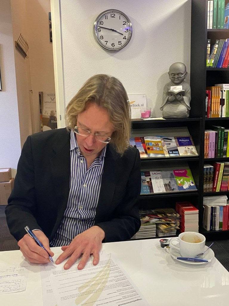 Frans van Hilten tekent het contract voor de roman 'Alles stroomt' op het kantoor van uitgeverij U2pi. Foto Jeroen van der Starre